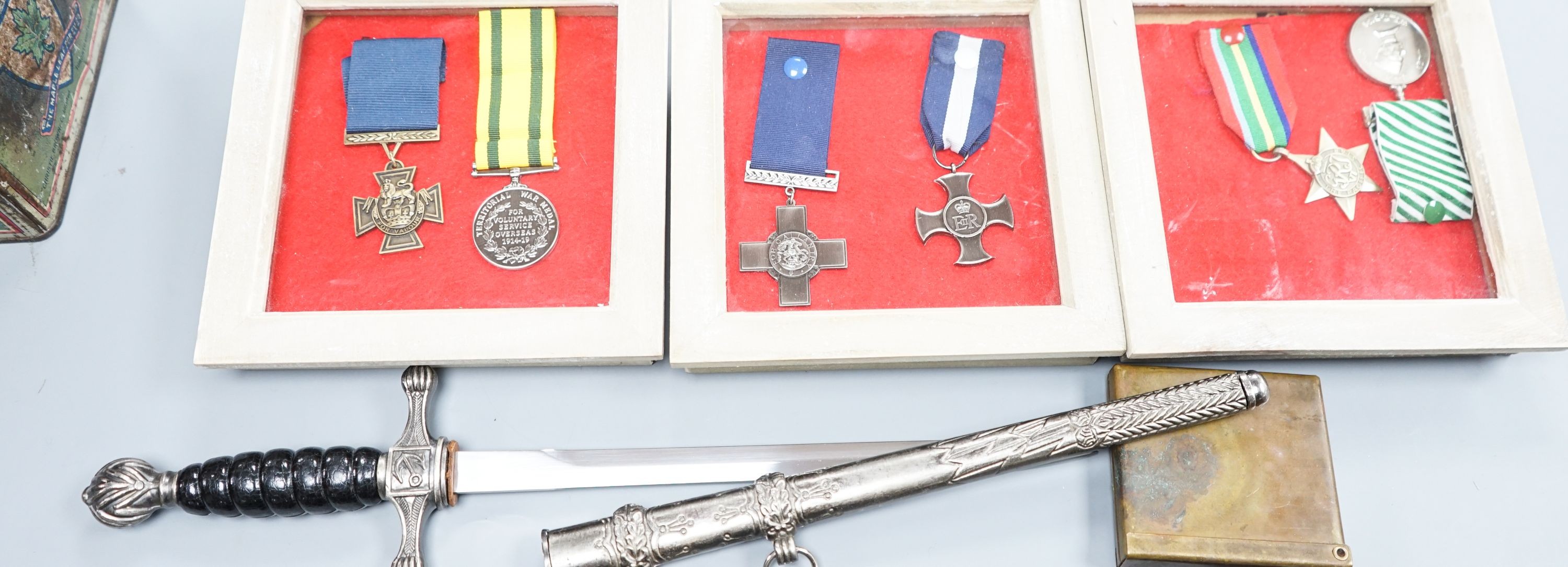 A Canadian First War Christie Brown and Co printed biscuit tin, framed medals, a trench art brass cigarette case and a reproduction German dagger.